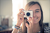 A blonde woman, smiling and cheerful taking a picture with a camera