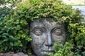 Garden statuary of a face with plants growing out of the top.