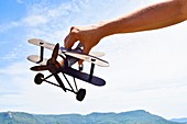 Close-up of  hand holding a model airplane against sky and mountain range.