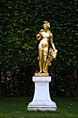 Golden statue of the hunting goddess Diana in front of a trimmed deciduous tree hedge in the Schwetzingen palace garden in late summer, Schwetzingen, Germany.