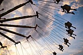 An amusement ride at a county fair sends riders soaring through the air at sunset.
