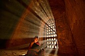 A young monk reading with rays of sunlight in the temples of Bagan, Myanmar.