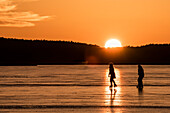 Silhouetten von Schlittschuhfahrern im Gegenlicht der roten, untergehenden Sonne auf dem Rangsdorfer See - Deutschland, Brandenburg, Rangsdorf
