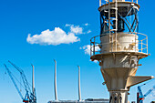 Ein historisches Leuchtfeuer und die Masten eines modernen Segelschiffes mit den Kränen einer Werft im Hafen, Kiel, Schleswig Holstein, Deutschland