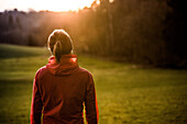 Junge Läuferin steht auf einem Feld bei einem Sonnenuntergang, Allgäu, Bayern, Deutschland