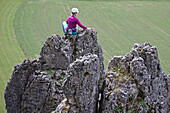 Junge Kletterin sitzt auf der Spitze eines hohen Felsens, Pottenstein, Franken, Deutschland