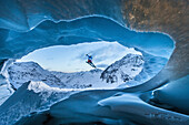 Junge Skifahrerin springt von einer Gletscherhöhle in den Bergen herunter/ Pitztal, Tirol, Österreich