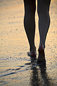 Woman walking on the beach at sunset.