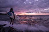Junge Surferin steht vor dem Meer während eines Sonnenuntergangs, Sao Tome, Sao Tome und Príncipe, Afrika