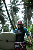 Young female surfer walking through a thick jungle, Sao Tome, Sao Tome and Principe, Africa