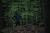 Junger Läufer macht eine Pause und betrachtet den Wald, Allgäu, Bayern, Deutschland