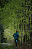 Junger Mann läuft auf einem Weg durch einen Wald, Allgäu, Bayern, Deutschland