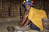 Traditionell gekleidete Zulu-Frau mahlt Getreide, Phe Zulu, Durban, KwaZulu-Natal, Südafrika