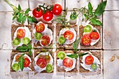 Presentation of slices of wholemeal bread with cheese and cherry tomatoes.