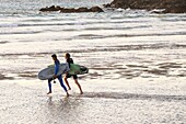 Two surfers running into the sea at Fistral beach in Newquay, Cornwall.