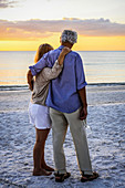 Retired couple enjoy a romantic walk on Siesta Key beach at sunset.