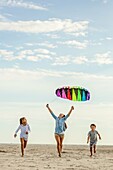 Two sisters and their brother fly a colorful kite on the beach. Coastal Georgia, USA