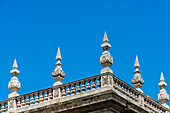 Ein Balkon mit Steingeländer und Steinobelsiken an einem historischen Gebäude vor blauem Himmel, Granada, Andalusien, Spanien