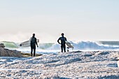 Surfers with boards survey the waves at Noord Hoek beach, Cape Peninsula, South Africa