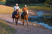 Two wranglers (cowboys) on horses, riding near a pond, California, USA