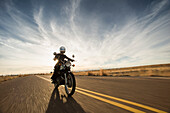 Sweeping wide and low angle perspective a woman riding the open road on her vintage motorcycle during sunset in Denver, Colorado