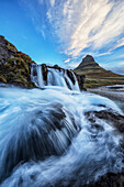 'A waterfall flows in the foreground of Kirkjufell, the most iconic and photographed mountain in Iceland; Iceland'