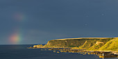 'Traces of a rainbow in the sky in the distance over the ocean with cliffs along the coastline; Cullen, Moray, Scotland'