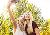 'Two sisters having fun outdoors in a city park in autumn and taking selfies of themselves when one sister covered the other sister's face with her hair; Edmonton, Alberta, Canada'