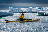 'Kayaker surrounded by icebergs resting his paddle; Antarctica'