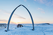 Whalebone arch frames the setting sun at the shore of the Arctic Ocean in Barrow, North Slope, Arctic Alaska, Winter