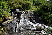 Man rides a full suspension mountain bike across a stream on the Devil's Pass Trail in the Chugach National Forest, Kenai Peninsula, South-central Alaska