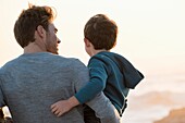 Happy father and son standing on the beach at sunset