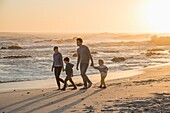 Happy young family walking on the beach at sunset