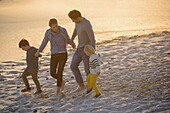 Happy young family walking on the beach at sunset