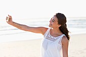 Happy young woman taking selfie with smartphone on the beach