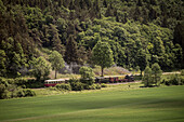 historical steam train passes Benedictine abbey at the so called Haertsfeld, Neresheim monastry, Ostalb district, Swabian Alb, Baden-Wuerttemberg, Germany