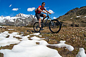 Biker cycles between snow and blooming Crocus in Val Fedoz, in the background Piz Lagrev in Engadine, Switzerland.