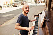 Hispanic man playing piano on city sidewalk