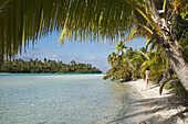 Aitutaki. Cook Island. Polynesia. South Pacific Ocean. A tourist walks along the edge of the palm-fringed beach in One Foot Island. Stamp Your Passport: Visit Aitutaki’s One Foot Island, where you’ll enjoy the incredible blue lagoon and a mouth watering b