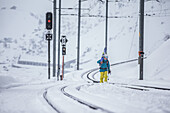 Junger Skifahrer läuft eine verschneite Eisenbahnschiene entlang, Andermatt, Uri, Schweiz