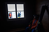 Junger Skifahrer betrachtet andere Skifahrer durch ein Fenster, Andermatt, Uri, Schweiz