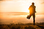 Young man running over a meadow at sunrise, Allgaeu, Bavaria, Germany