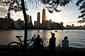 United States, Illinois, Chicago, Gold Coast and buildings at the edge of Michigan Lake at sunset seen from Olive Park, silhouetted bike and man taking a picture with his mobile