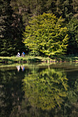 Woman and man ride bicycles on path along Aubachseen lakes, Habichsthal, Spessart-Mainland, Bavaria, Germany