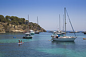 Two young women on paddleboard with yachts and sailboats at anchor in Cala Portals Vells bay, Portals Vells, Mallorca, Balearic Islands, Spain
