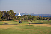Golfer auf Fairway von Golfplatz Club de Golf Alcanada mit Leuchtturm Faro de Alcanada im Hintergrund, nahe Port d'Alcudia, Mallorca, Balearen, Spanien