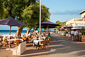 People sit outside at Es Vivers restaurant on beach promenade, Colonia de Sant Pere, Mallorca, Balearic Islands, Spain