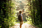 Caucasian woman photographing forest trees with cell phone