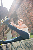 Caucasian woman tying roller skate near brick wall