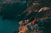 Caucasian woman sitting on rocks at ocean